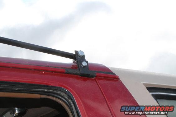 Red and tan SUV roof rack mount with bolts against a cloudy sky