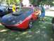 1970 Ford Ranchero - A man inspects an orange sports car with a black hood and scoop at an outdoor car show.
