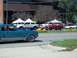 1970 Ford Ranchero - A blue coupe drives past several trucks and a white convertible at an outdoor event.