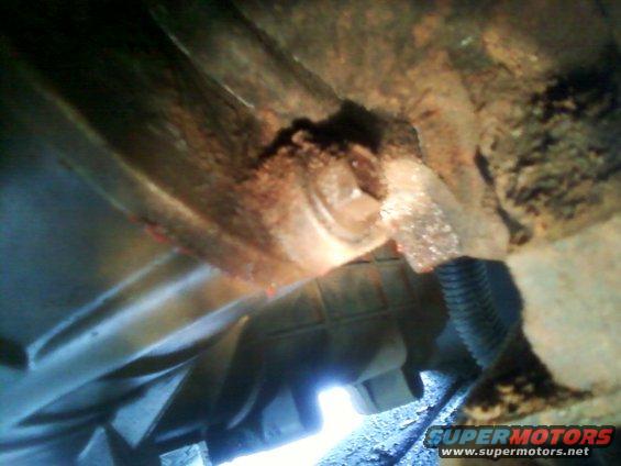 Close-up of a rusty, damaged vehicle transmission housing with a black hose