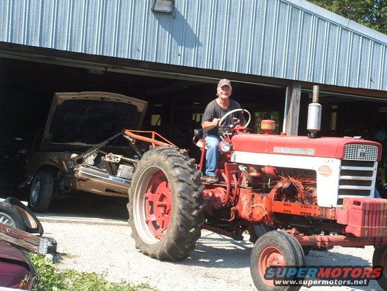 Man on red tractor towing a gold car chassis with hood open