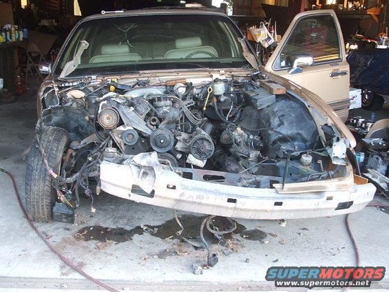 Tan car with front end disassembled, showing engine and wiring
