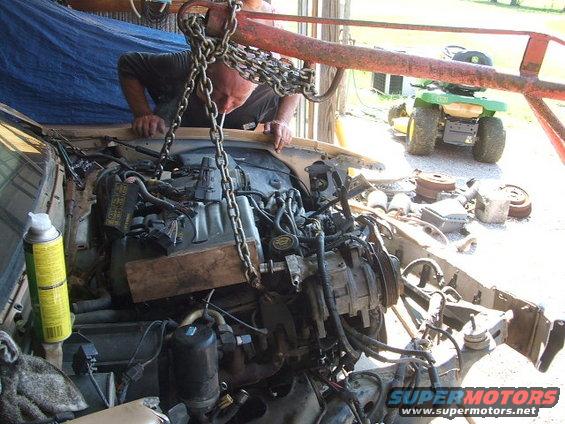 Engine bay with chains and engine hoist; lawn tractor in background