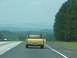 1972 Ford Ranchero - A yellow pickup truck with prominent dual exhaust pipes is seen from behind on a highway.