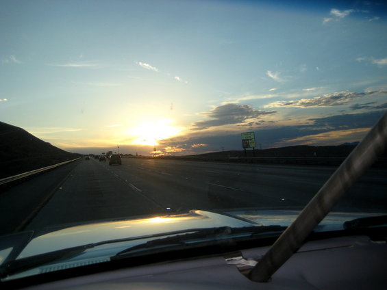 View from inside a vehicle looking out at a highway during sunset with a billboard visible