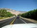 1996 Ford Bronco - A blue pickup truck tows a trailer down a highway, with mountains and trees lining the road under a clear blue sky.