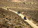 1996 Ford Bronco - Multiple off-road vehicles navigate a winding dirt path in a desolate, arid landscape.
