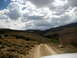 1996 Ford Bronco - A dirt road leads through a barren valley with green vegetation in the distance, under a dramatic sky.