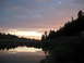 1996 Ford Bronco - A campsite is set up by a lake, with tents and vehicles visible as the sun sets over the horizon.