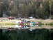 1996 Ford Bronco - A group of off-road vehicles and tents are set up near a reflective lake in a wooded area.
