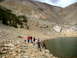 1996 Ford Bronco - Several people gather by the edge of a clear lake, with a steep, rocky mountainside dominating the background.