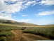 1996 Ford Bronco - Two vehicles traverse a dusty trail in a wide, open, arid landscape with rolling hills under a partly cloudy sky.