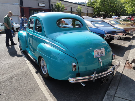 Teal coupe with chrome bumper and dual exhaust pipes, parked on asphalt