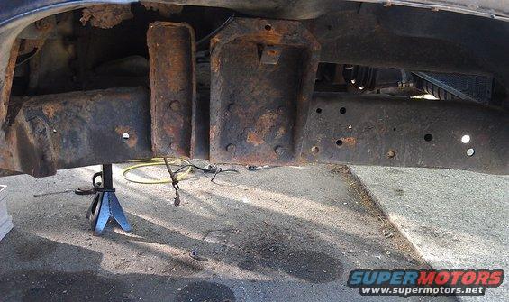Heavily rusted truck frame and suspension parts supported by a blue jack stand