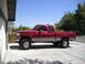1997 Ford F-250 - A red 1997 Ford F-250 pickup truck is shown from the side, lifted with large tires.