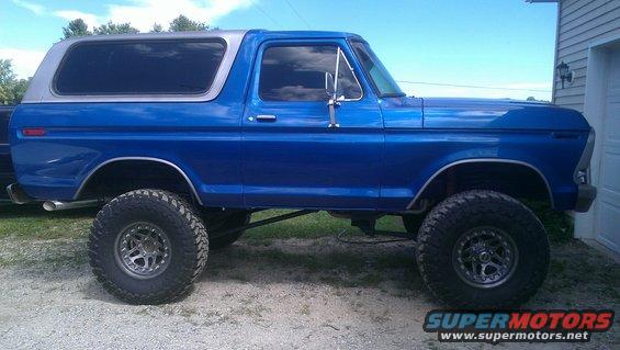 Blue 1978 Ford Bronco with silver roof, lifted suspension, and chrome wheels parked next to a garage