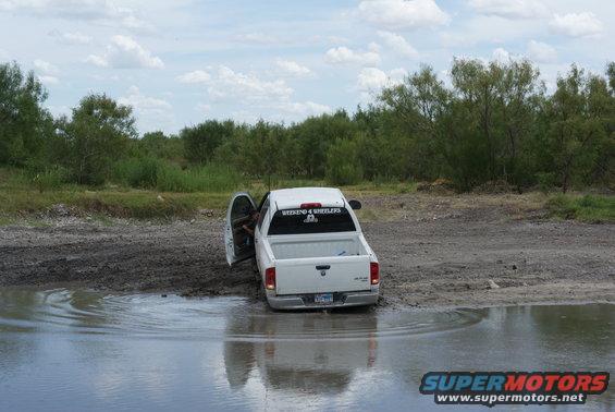 White pickup truck stuck in mud and water, driver's door open