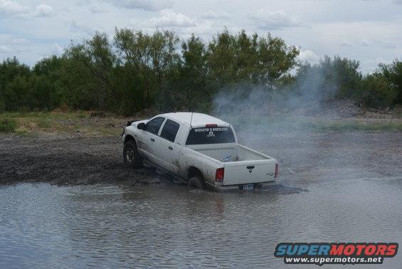White pickup truck stuck in mud and water, with smoke coming from the rear
