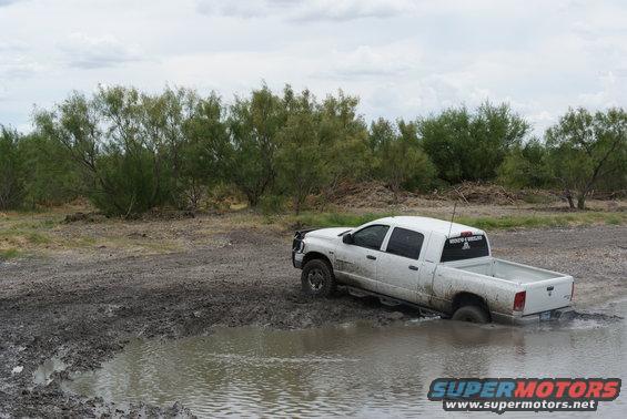 White pickup truck stuck in a muddy puddle, rear passenger side submerged