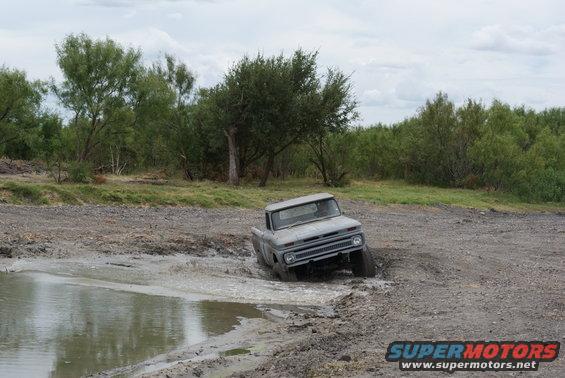 Gray pickup truck stuck in mud, front 3/4 view. Grille and headlights visible