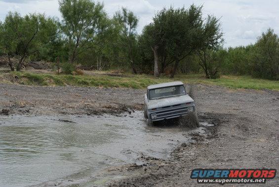 Gray 1966 pickup truck driving through mud puddle, front 3/4 view