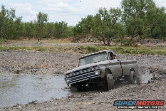 Gray pickup truck driving through a muddy puddle. Driver visible