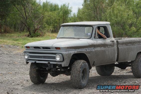 Muddy old pickup truck with big tires, driver's arm out the window