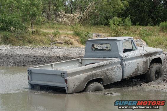 Gray 1960s pickup truck stuck in mud, rear-wheel drive submerged