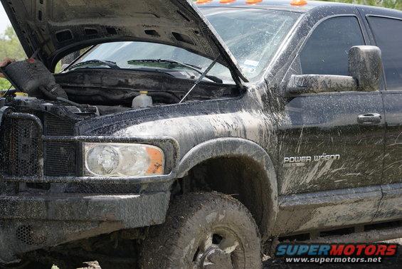 Mud-covered black pickup truck with hood open, showing engine and front grille