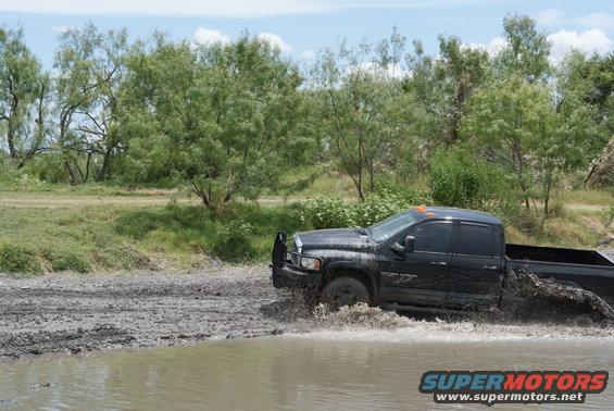 Black pickup truck driving through mud and water, front bull bar visible