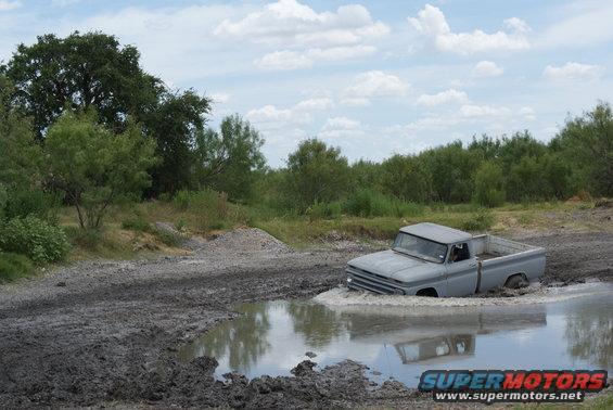 Gray pickup truck stuck in mud puddle, front 3/4 view