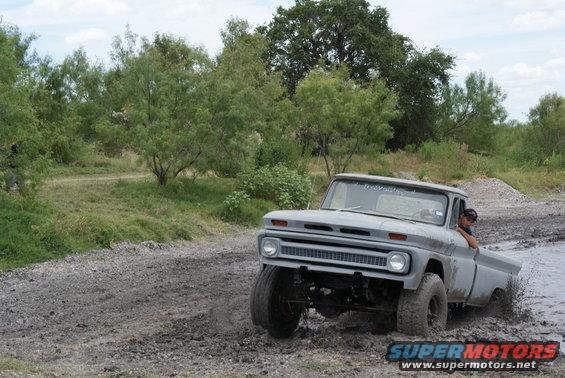 Gray 1966 pickup truck driving through mud, front 3/4 view