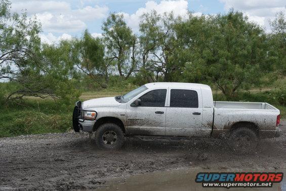White pickup truck with crew cab driving through a muddy puddle, splashing water