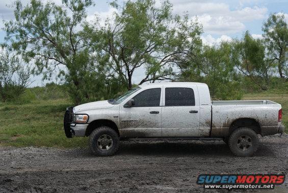 White pickup truck with four doors parked on a dirt road, trees and brush in the background