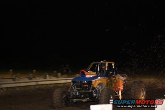Monster truck with roll cage, large tires, and custom paint job driving on dirt at night