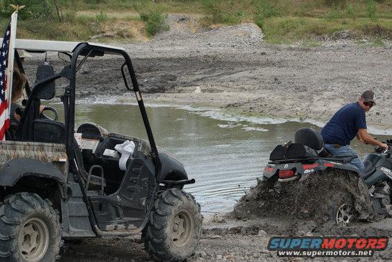Side-by-side UTV with American flag stuck in mud next to ATV
