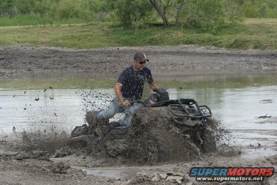 Man riding an ATV through a muddy puddle, splashing water
