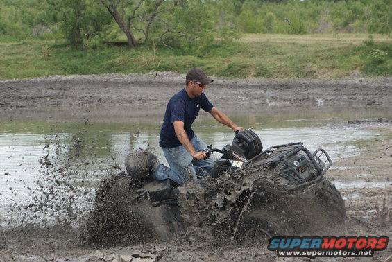 Black ATV splashing mud with a rider on it in a muddy field