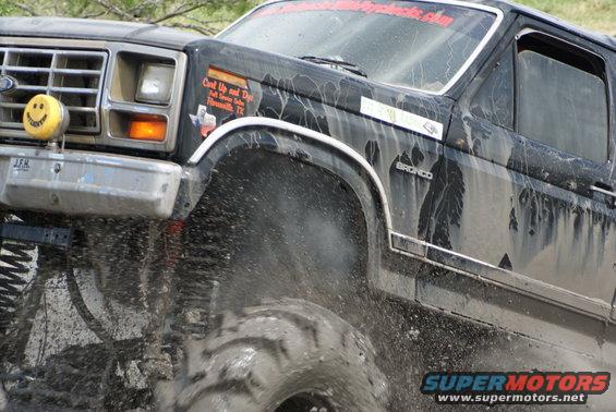 Mud splattering from tire of a black Ford Bronco, "BRONCO" badge visible on fender