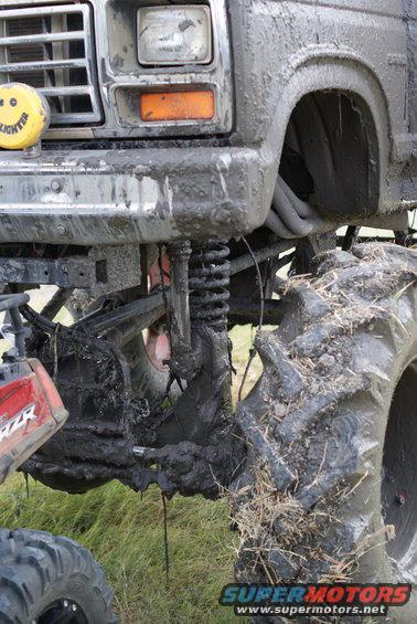 Mud-covered front end of a lifted 1980s truck with large tires and visible suspension
