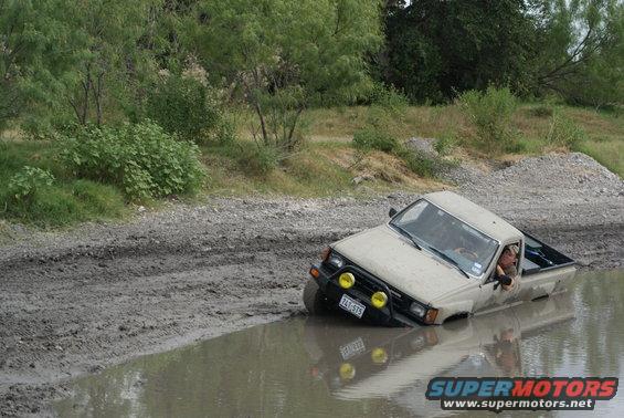 Tan Toyota pickup truck stuck in muddy water, front end submerged