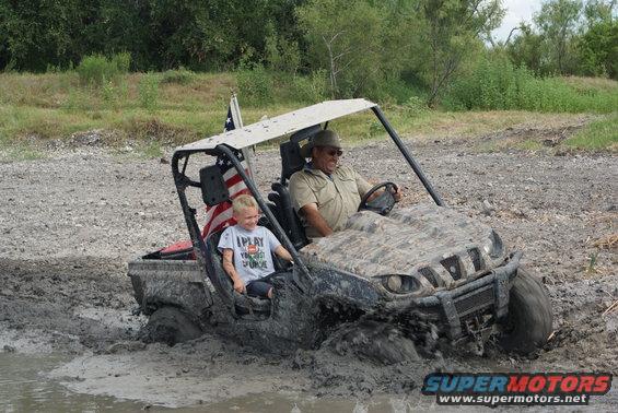 Mud-splattered side-by-side utility vehicle with two people driving through mud