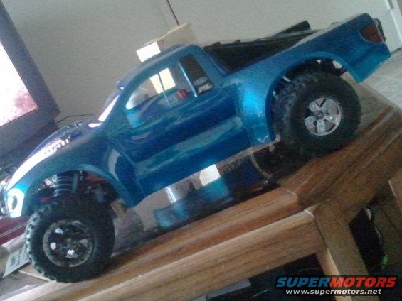 Blue remote control truck body on wooden ramp, showing suspension and tires