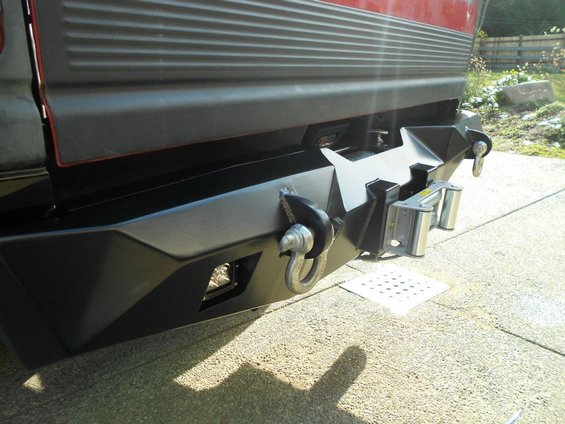 Aftermarket rear bumper with winch, tow hooks, and roller fairlead mounted on a vehicle