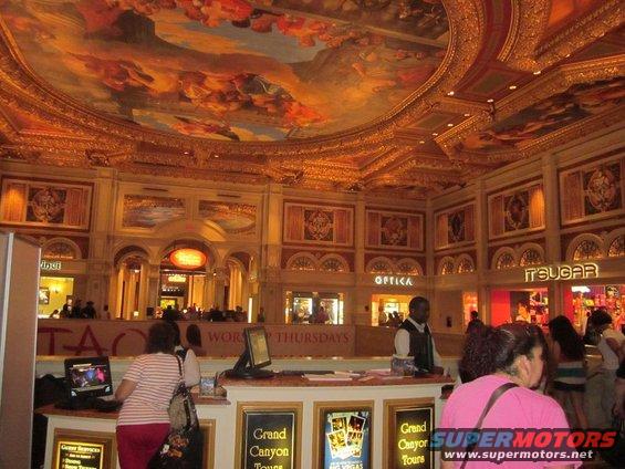 Interior of a casino lobby with ornate ceiling and shops like Optica and It'Sugar