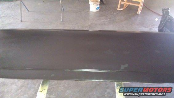 Dark car door on a stand, showing primer and some scuffs