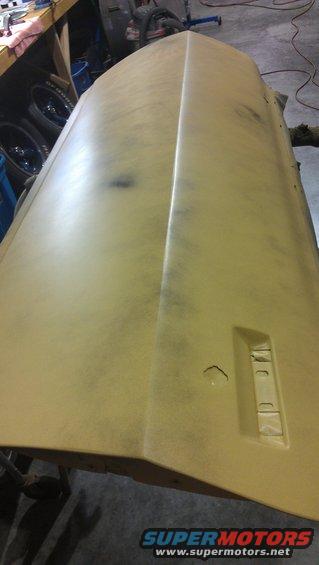 Car hood covered in primer, showing a central crease and a rectangular recess on the right side