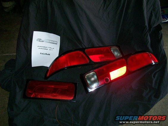 Three red Ford Probe GT taillights and a paper with text on a black cloth background