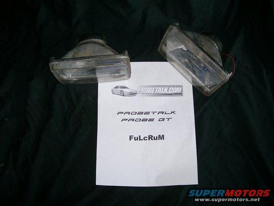 Pair of clear plastic fog lights with a document showing 'PROBETALK PROBE GT' and 'FuLcRuM'