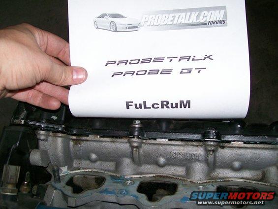 Hand holding a paper with "PROBETALK PROBE GT" text over an engine part